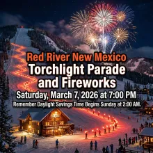 A dramatic nighttime winter landscape at Red River Ski Resort featuring a glowing trail of skiers with red torches descending a snowy mountain toward a rustic, warmly lit Lift House. The dark sky is filled with vibrant, colorful fireworks. Bold text overlays the scene: "Red River New Mexico Torchlight Parade and Fireworks. Saturday, March 7, 2026 at 7:00 PM. Remember Daylight Savings Time Begins Sunday at 2:00 AM."